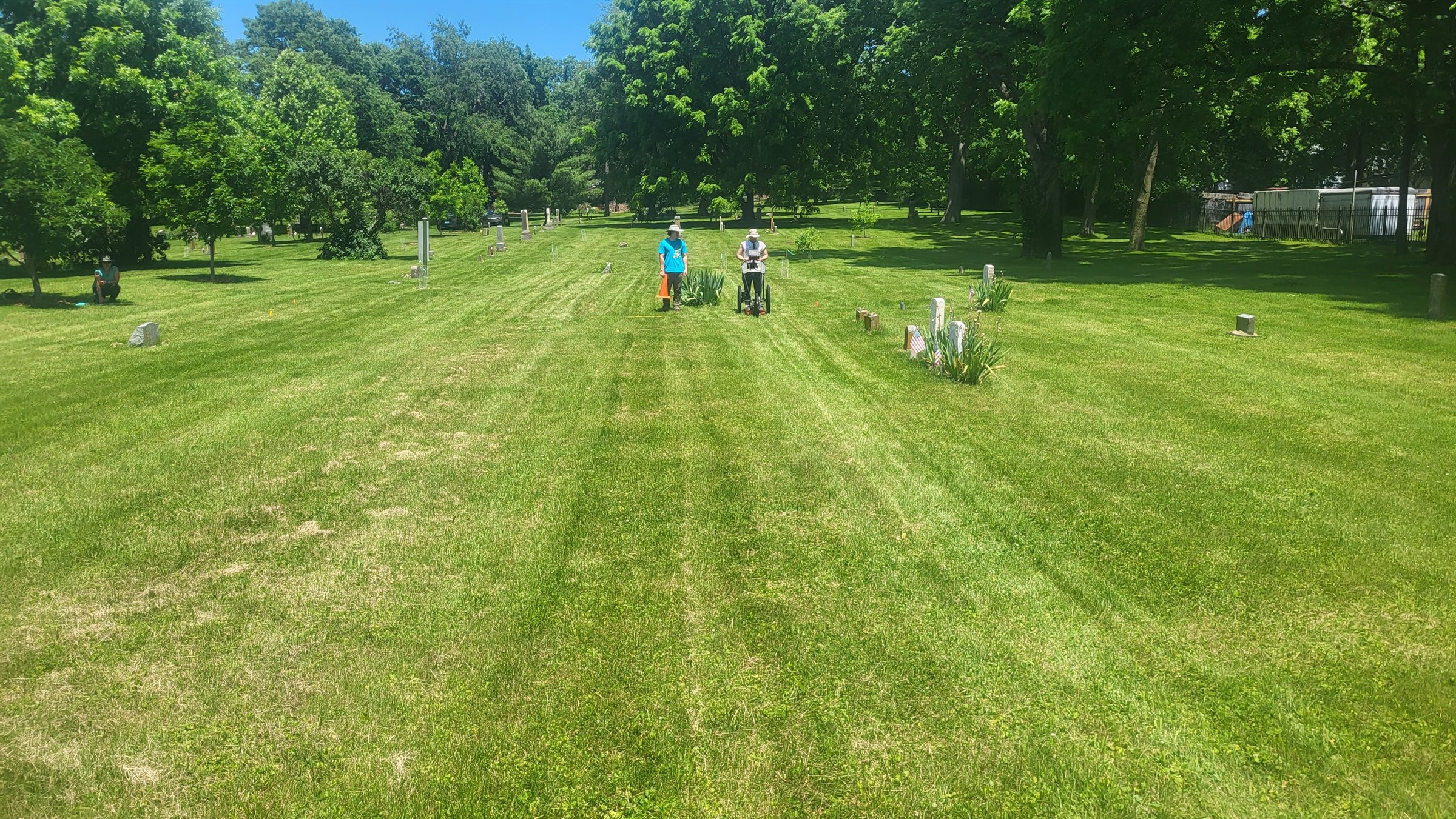 A researcher pushing a ground-penetrating radar cart across mown grass between scattered headstones at African Cemetery No. 2, Lexington