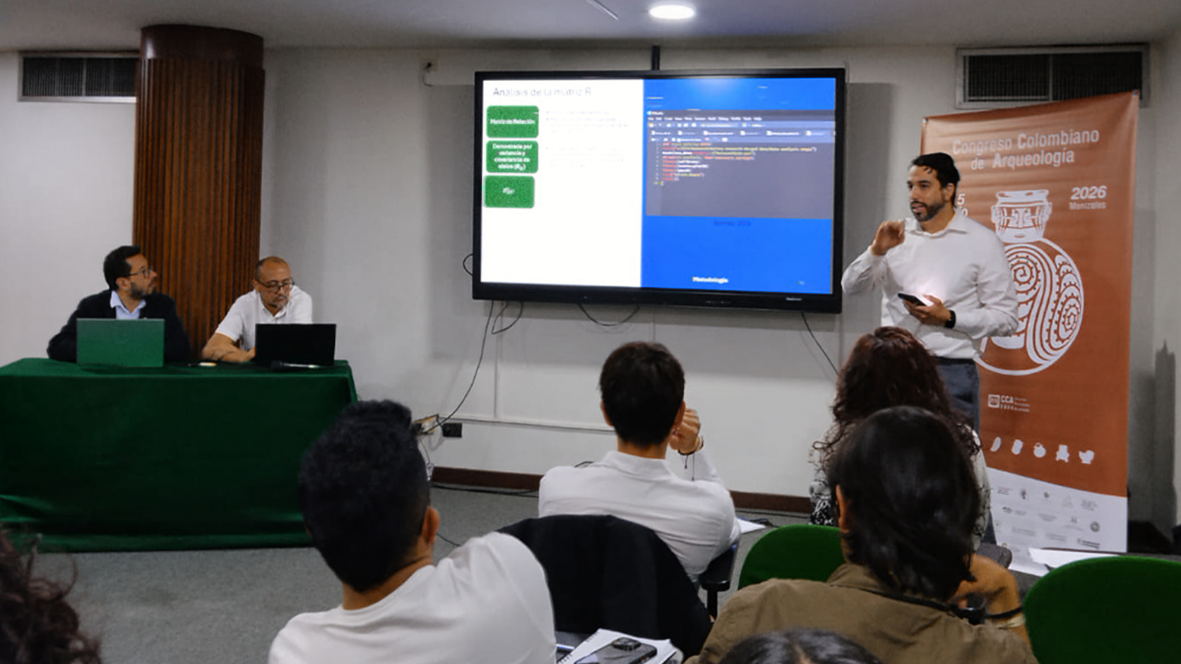 Daniel Benítez presenting beside the Congreso Colombiano de Arqueología 2026 banner in Manizales, Colombia