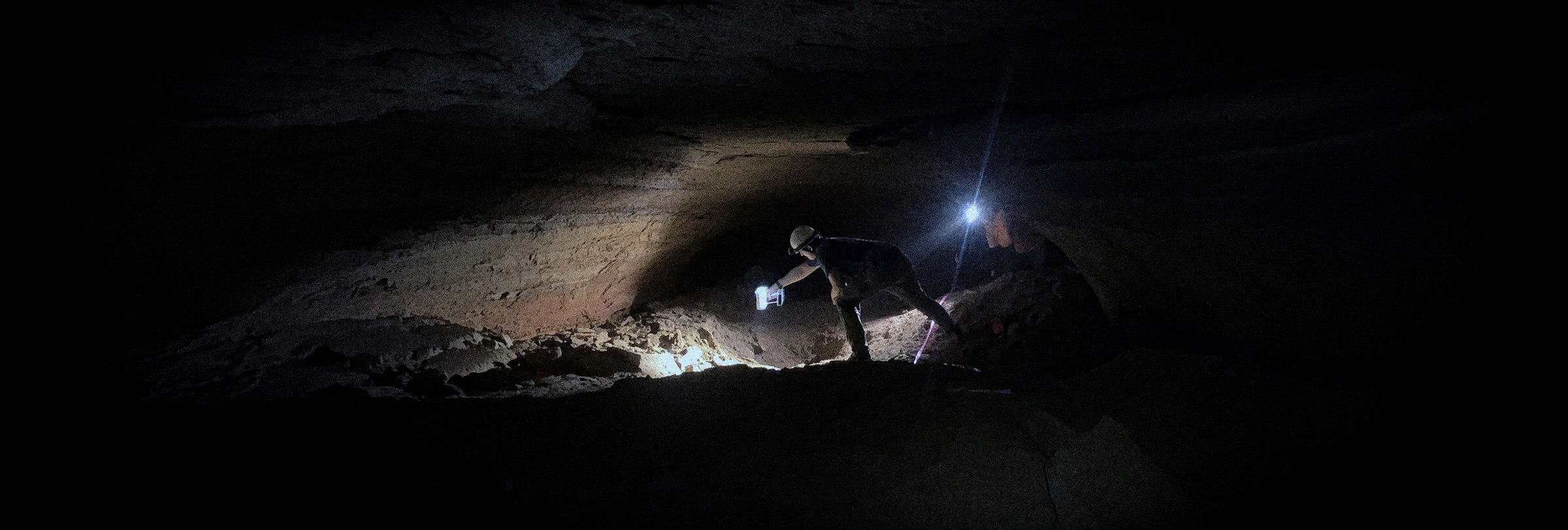 James Keppeler operating a handheld 3D scanner over human trackways on the floor of Helms Deep Cave, lit by headlamp