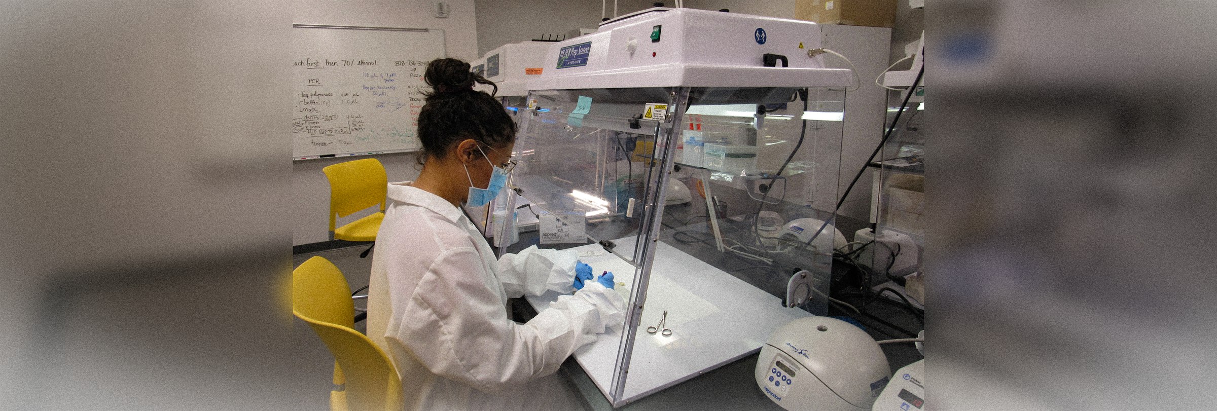 A HEVA researcher in a lab coat, mask and gloves preparing samples at a PCR workstation